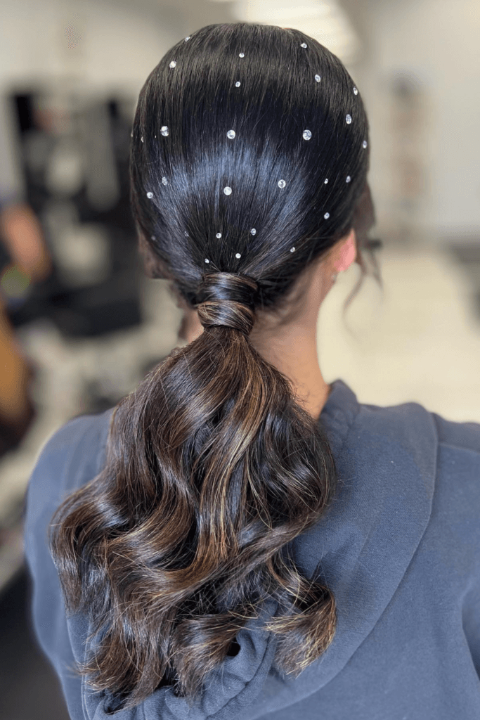 Sleek low ponytail adorned with pearl pins and finished with glossy, defined curls.