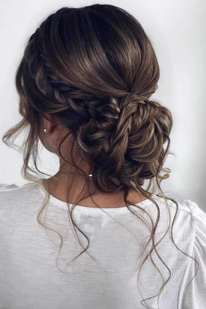 Side braid feeding into a messy low bun on brown hair with loose tendrils