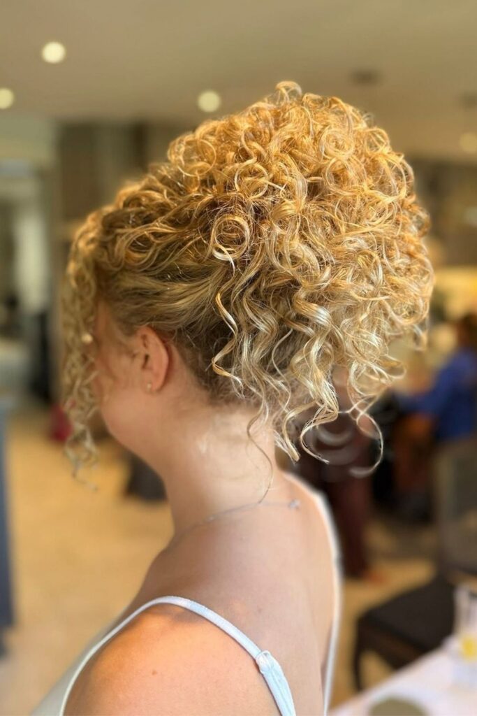 Natural blonde curls pinned into a high updo, a hoco hairstyle for curly hair