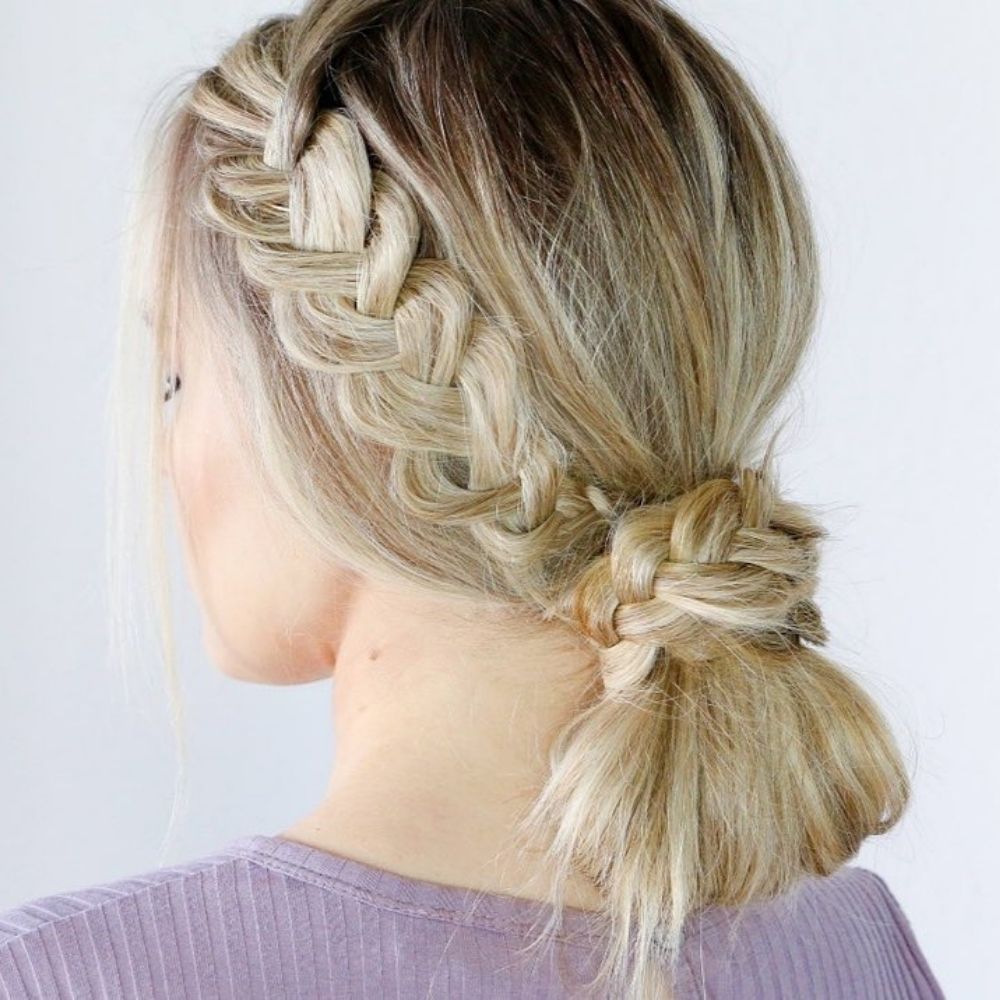 Side Dutch braid tied into a knotted low bun on blonde hair