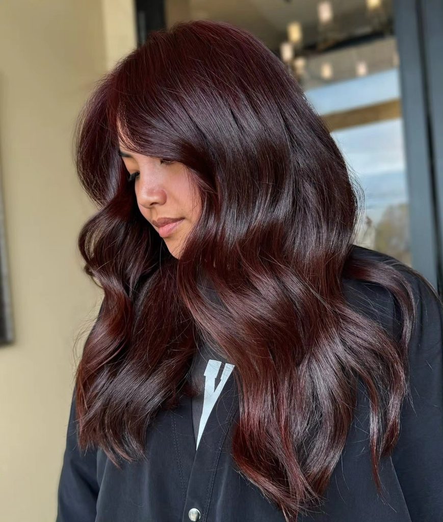 Side profile of long wavy cherry brunette hair with deep red undertones, an example of fall red hair with movement and shine.