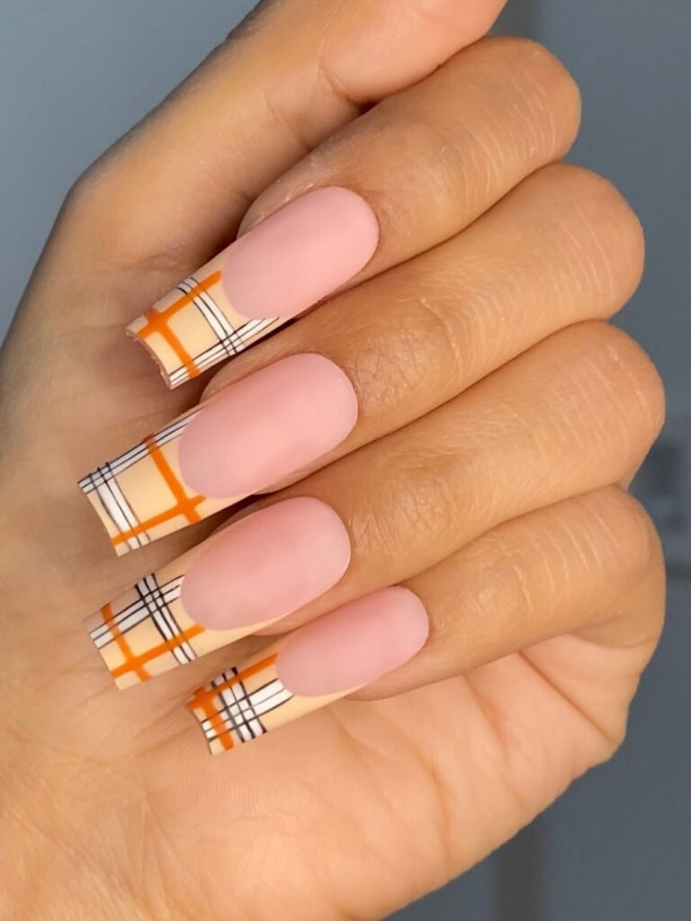 Long square nails with matte nude bases and structured plaid French tips in orange, cream, and black.