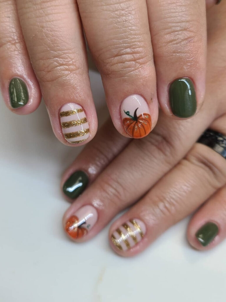 Short round nails in deep olive green with gold glitter stripe accents and one hand painted orange pumpkin.