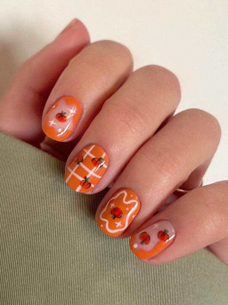 Short squoval nails in bright pumpkin orange with white squiggles, white plaid, and clusters of tiny hand painted pumpkins.