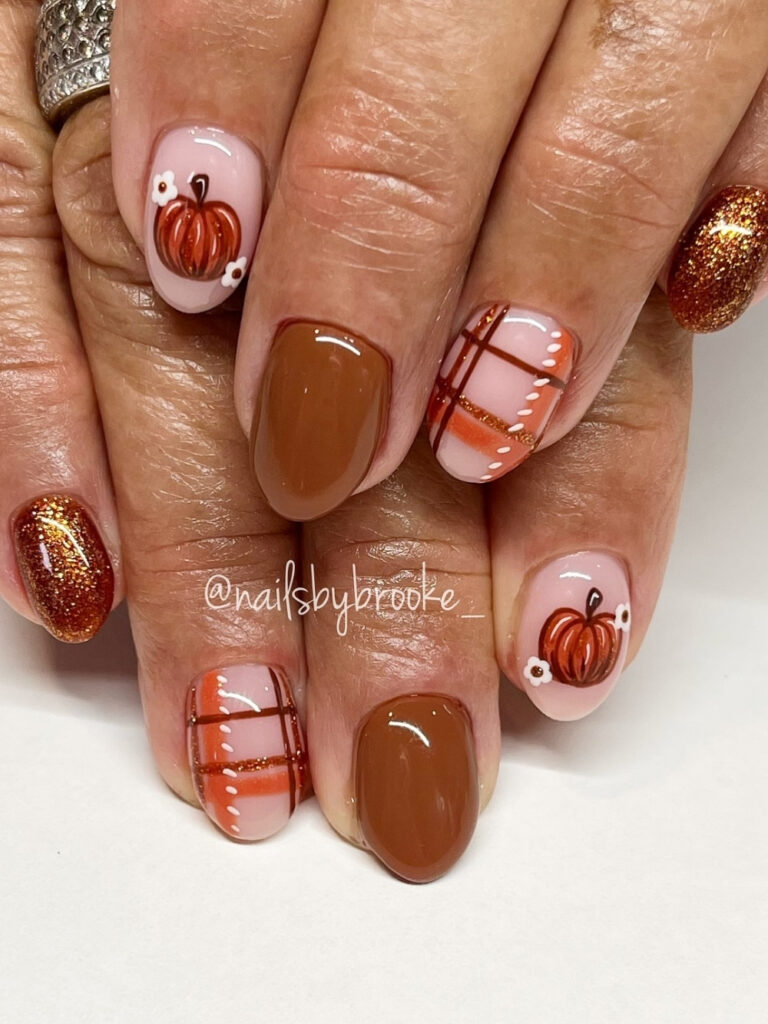 Pumpkin nails on short round tips in caramel brown and copper glitter, with hand painted orange pumpkins, white daisies, and plaid accents.