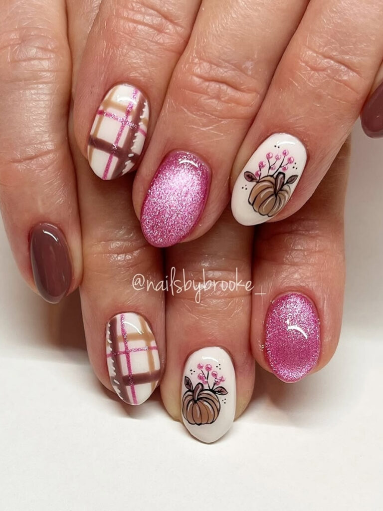 Short round nails in mauve and hot pink glitter with plaid accents and a white nail featuring a hand painted pumpkin with pink berry sprigs.