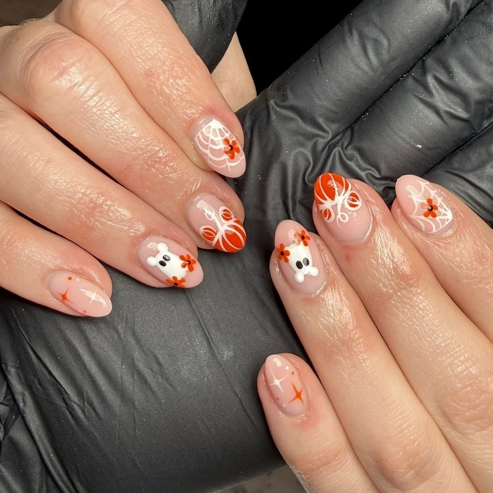 Medium almond nails on sheer nude with 3D white ghosts, hand painted spiderwebs, orange flowers, and a striped pumpkin.