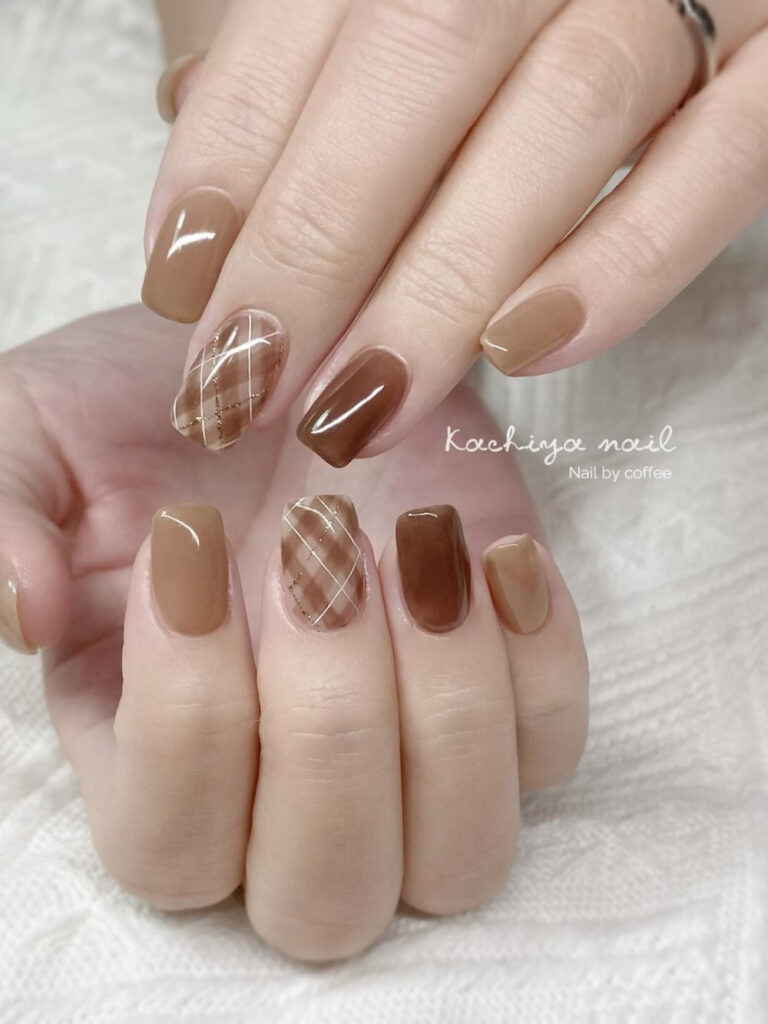 Short square nails in alternating caramel and milk chocolate shades with a sheer argyle plaid accent nail traced in gold.