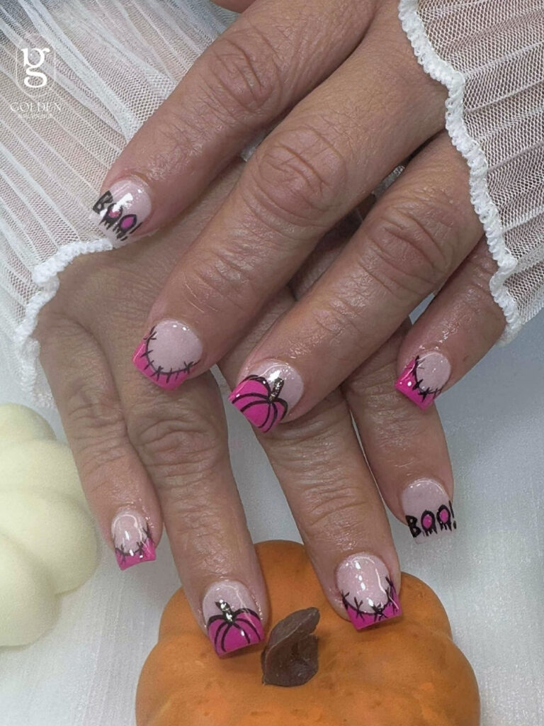 Short square nails with shimmery pink bases, hot pink French tips, hand painted pumpkins, stitched smile details, and BOO lettering.