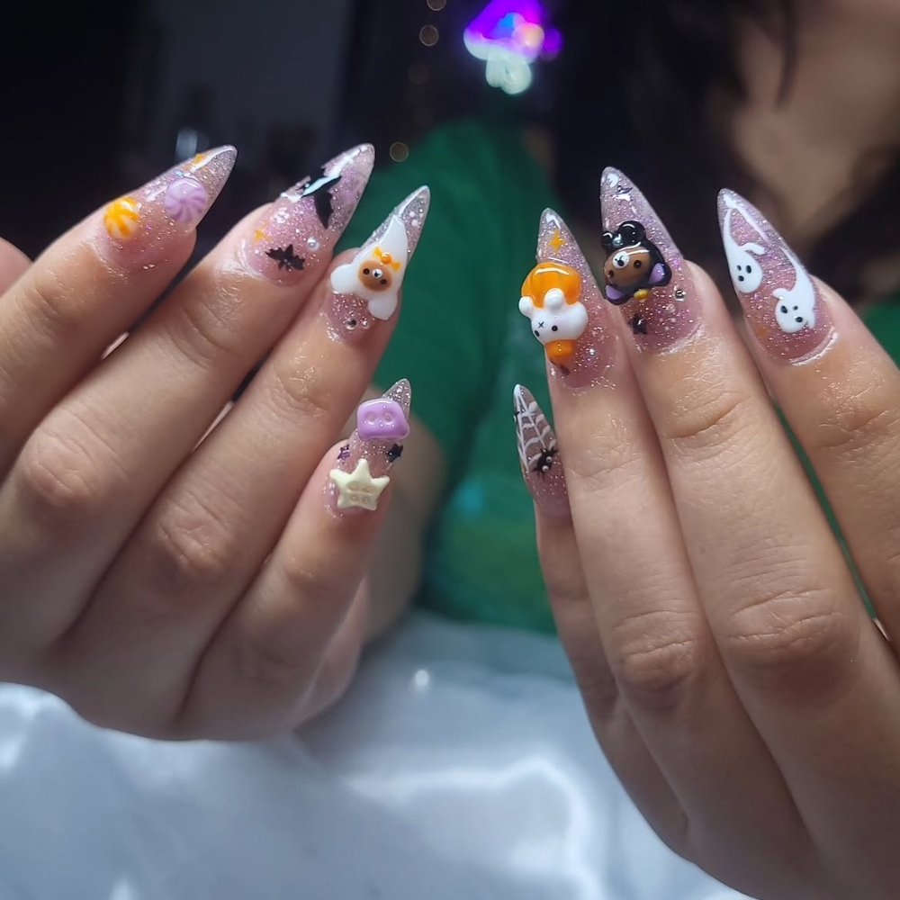 Long stiletto nails in sheer lilac glitter jelly with 3D charms including ghosts, bats, bears, pumpkins, stars, and spiderwebs.