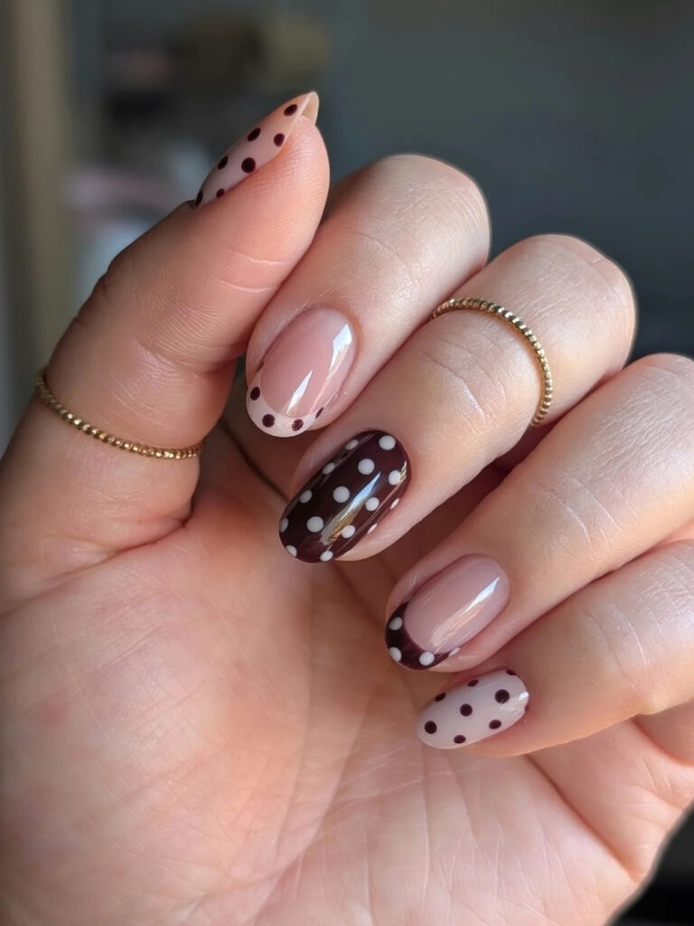 Short almond nails alternating between a dark brown base with white dots, a nude base with brown dots, and dotted French tips.