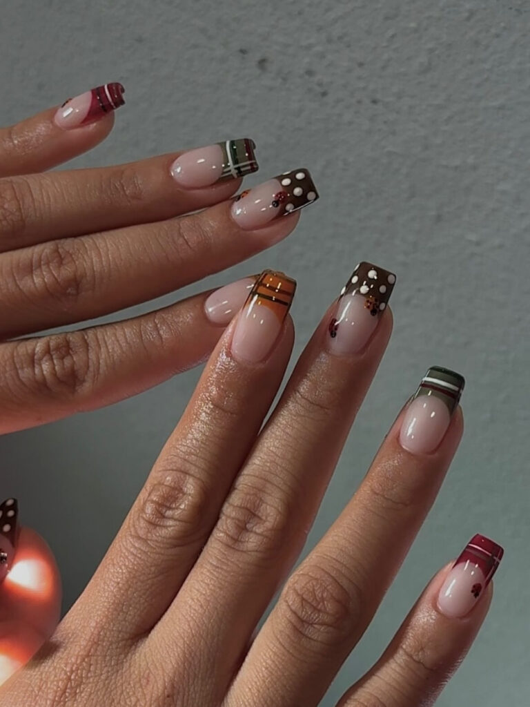 Plaid nails on medium square tips, with sheer pink bases and mismatched plaid French tips in burgundy, forest green, orange, and brown plus polka dot accents.
