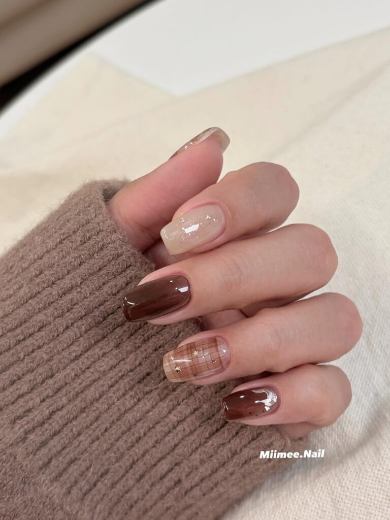 Medium square nails in cinnamon and deep brown with a sheer plaid accent nail scattered with gold star charms and fine glitter.