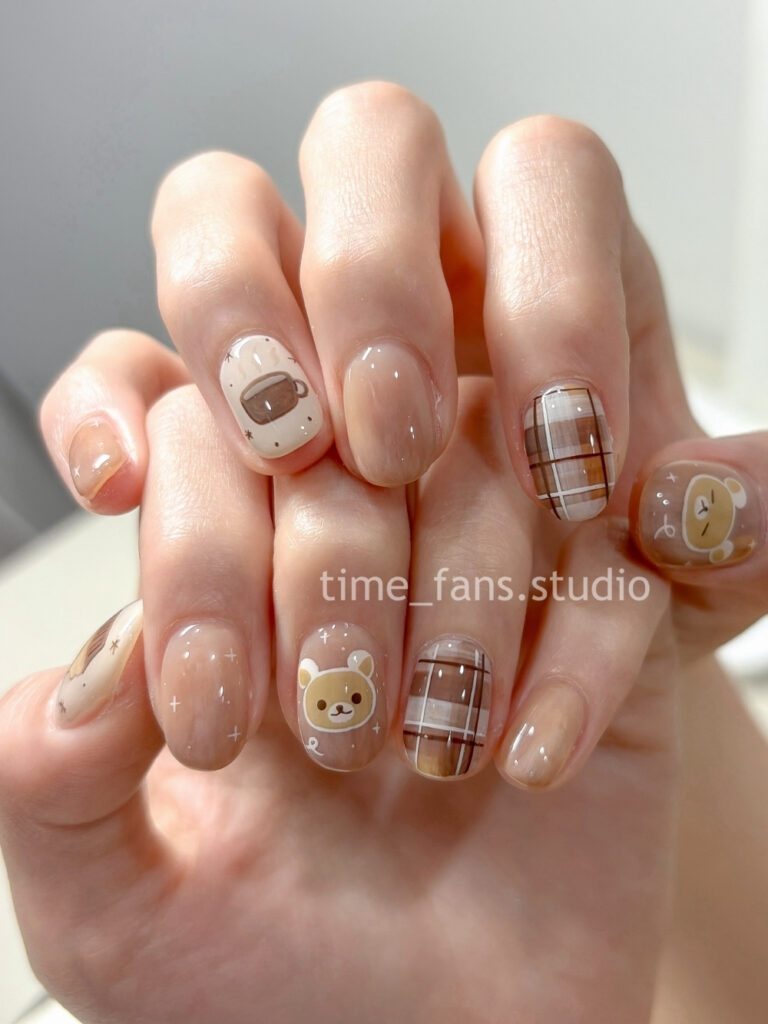 Short round nails in milky beige with a hand painted teddy bear, a steaming coffee cup, and brown plaid accents.