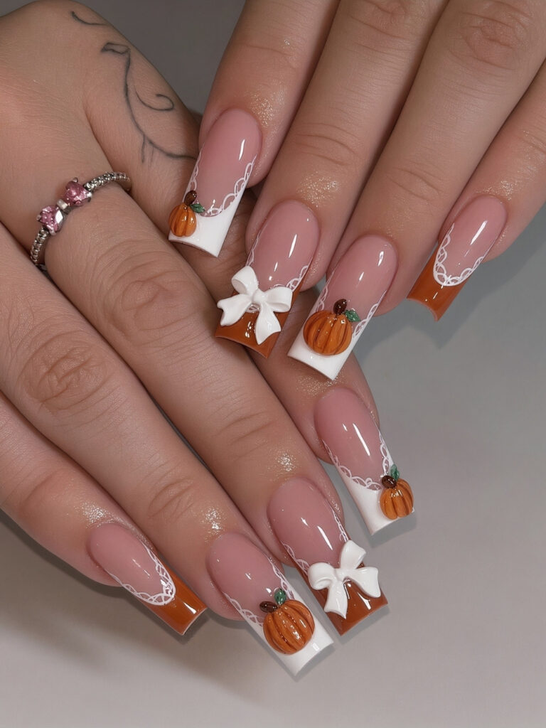 Long square nails with white and burnt orange French tips, delicate lace detailing, and raised 3D pumpkins and white bows.