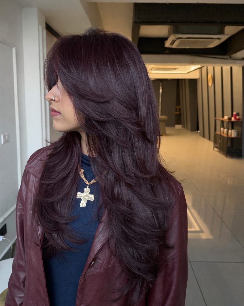 Side profile of long layered dark wine red hair styled with soft waves and face-framing layers, a dramatic dark fall hair color.
