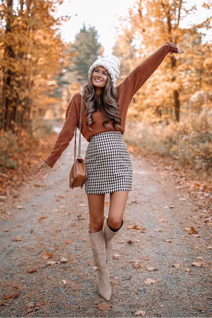 Gingham mini skirt with rust sweater and tall boots surrounded by fall foliage