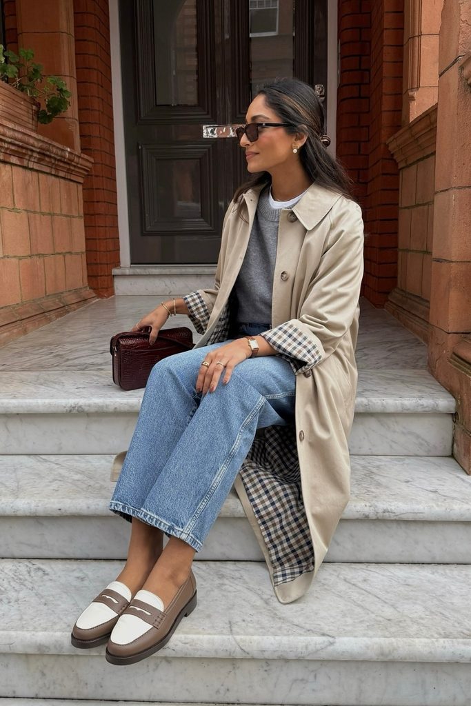 Beige trench coat with checked lining worn over jeans, a classic early fall outfit