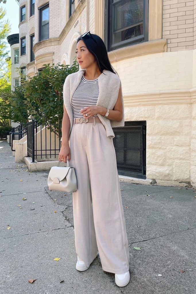 Woman wearing a striped tee, cream sweater vest, and wide-leg trousers for an early fall outfit