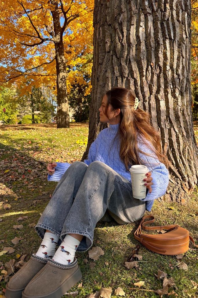 Periwinkle cable knit sweater and jeans outfit surrounded by autumn leaves