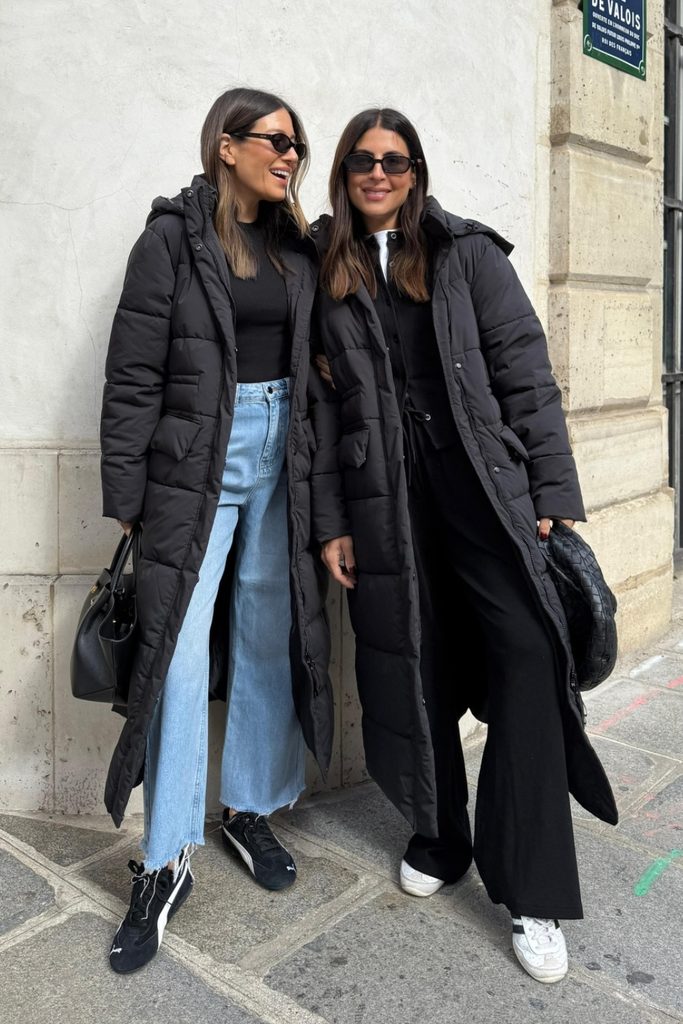 Two friends wearing long black puffer coats with jeans and sneakers