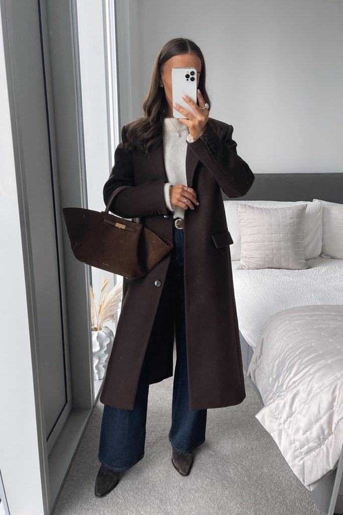 Long chocolate brown coat with dark denim jeans and a cream sweater