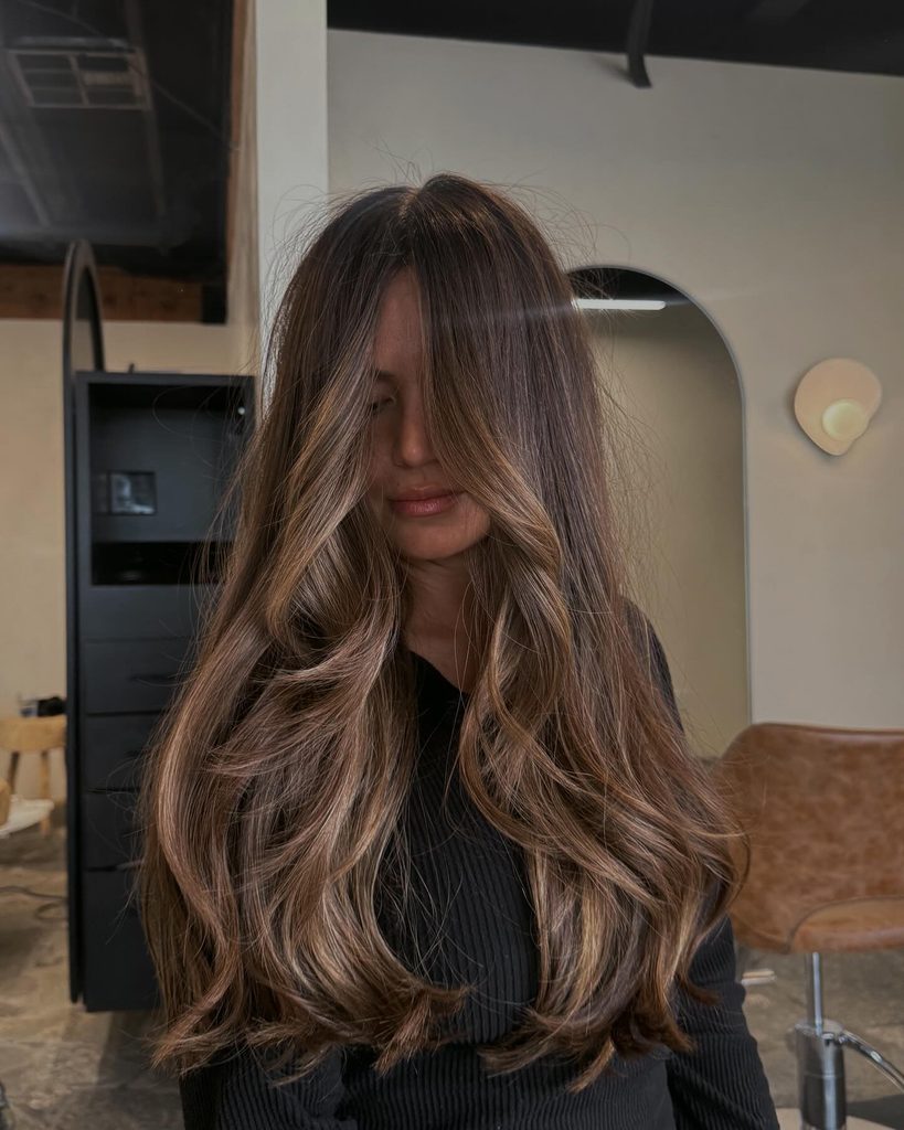 Front view of long wavy dreamy brunette balayage hair falling over the face, a dimensional fall hair color for brunettes.