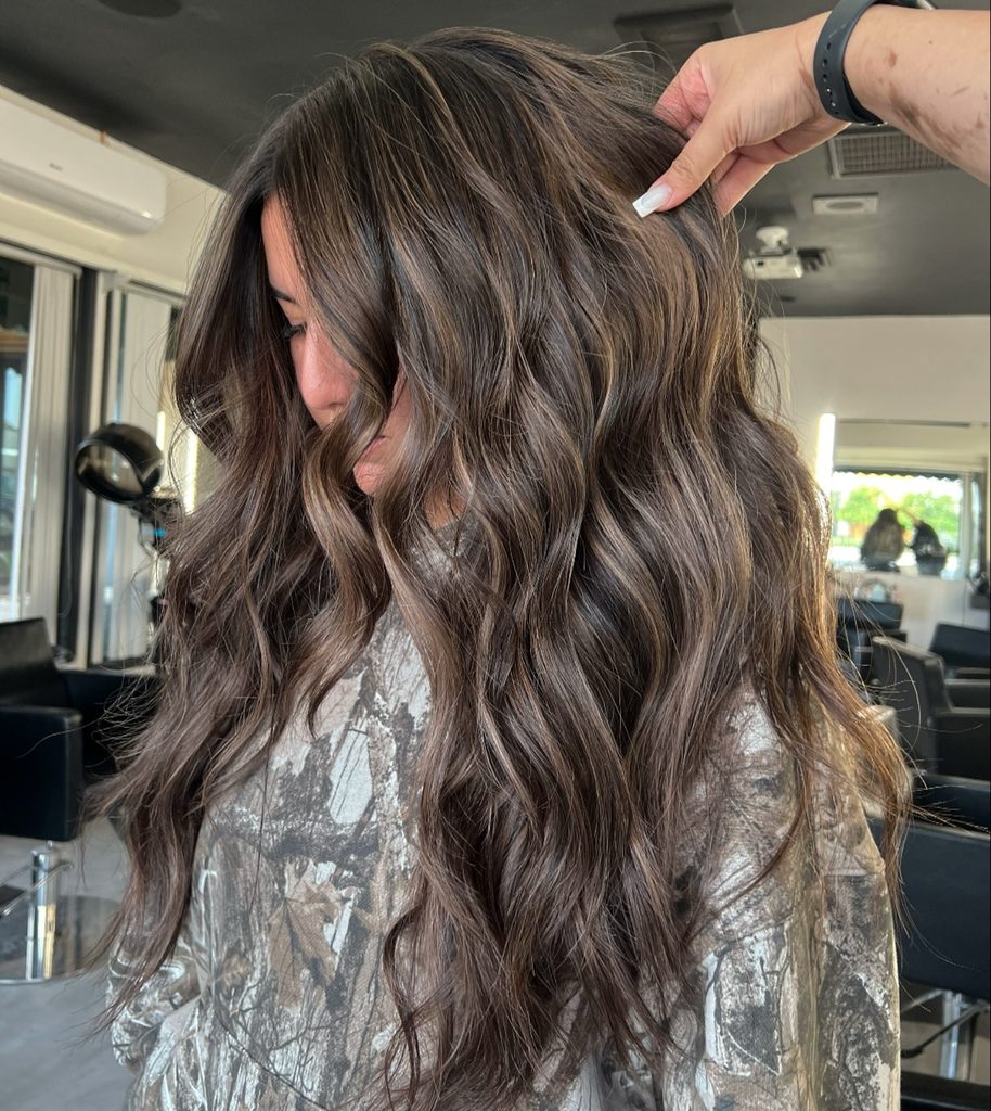 Side view of wavy beige brunette balayage hair with warm caramel highlights, a subtle fall highlights for brown hair look.