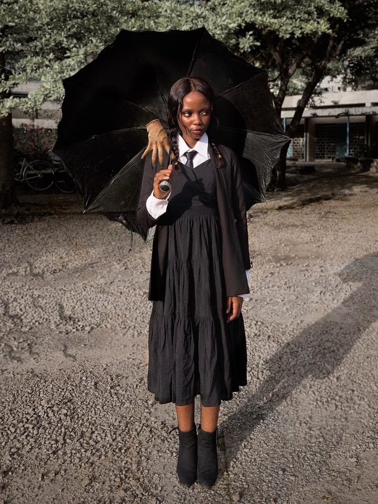Woman wearing a black cardigan and braided pigtails in a Wednesday Addams-inspired costume