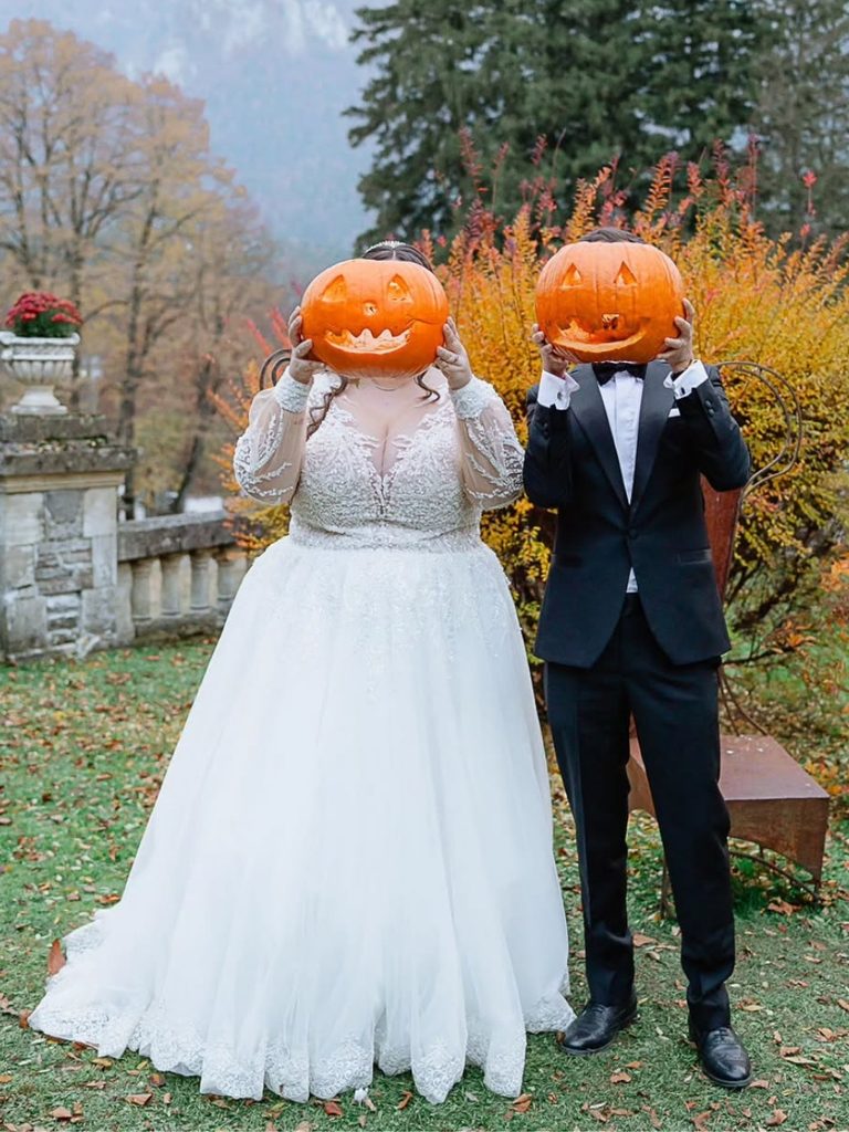 Bride and groom in formalwear holding carved pumpkin heads.