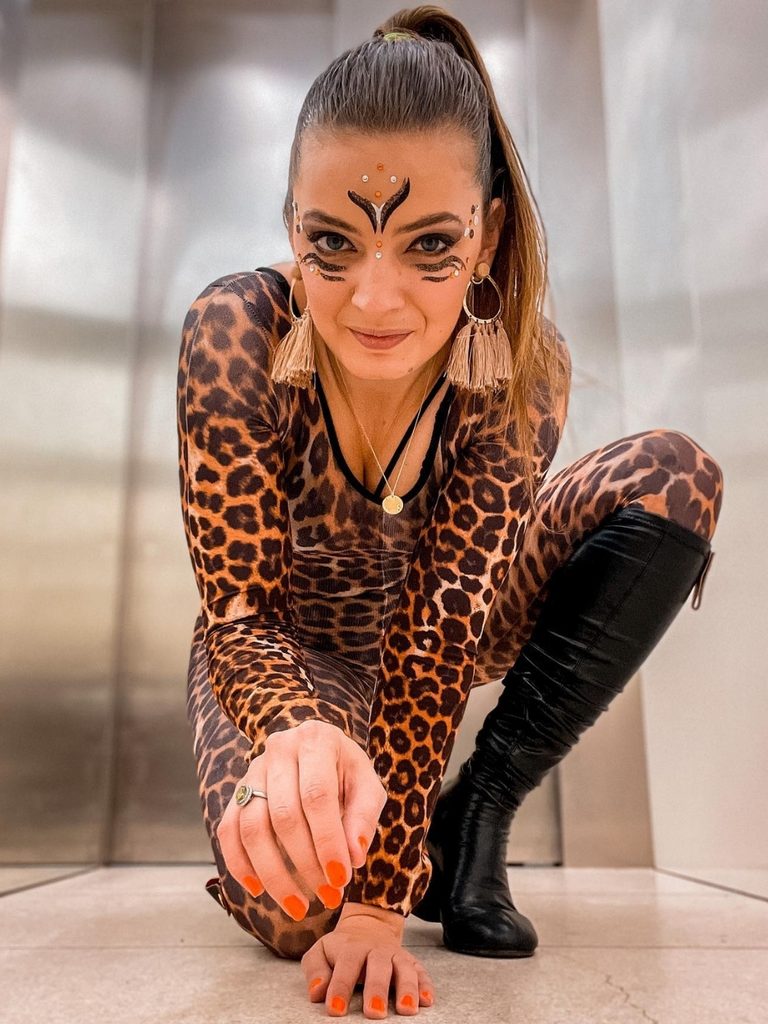 Woman wearing a leopard print bodysuit, tall boots, and face paint.