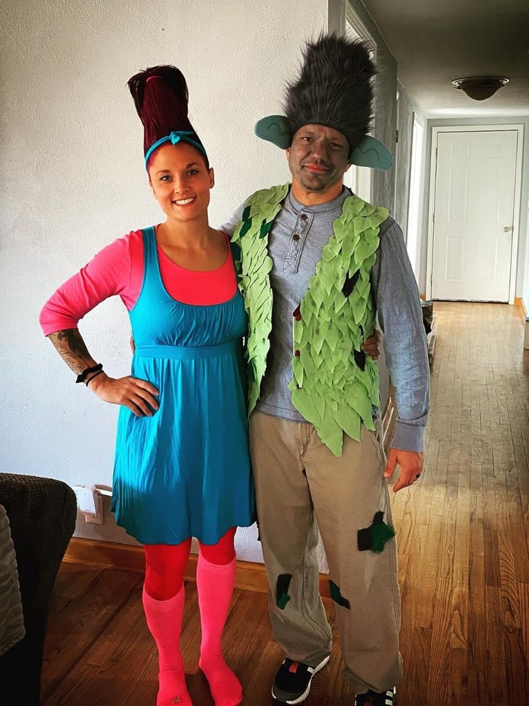 Couple dressed as Poppy and Branch from Trolls in colorful outfits.