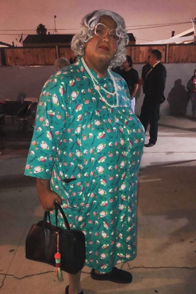 Person dressed as a comedic grandma character in a floral housedress and gray wig.