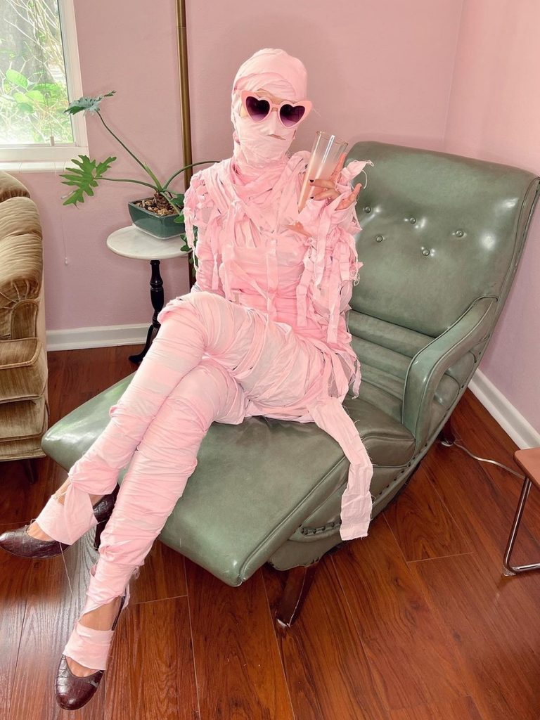 Woman wrapped in pastel pink fabric strips for a mummy-inspired look.