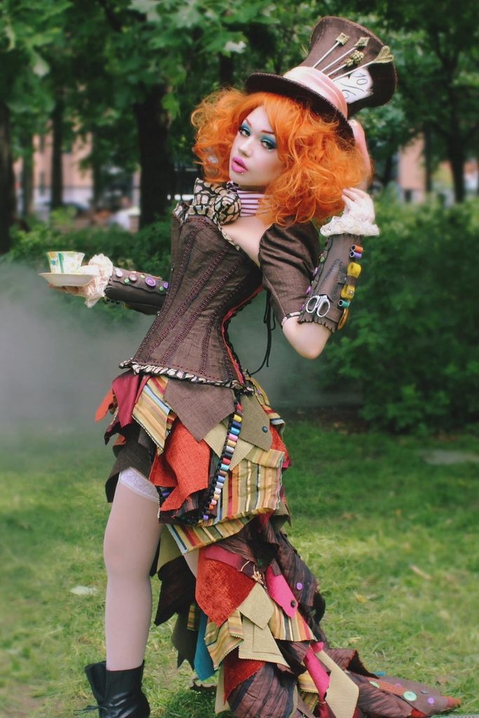 Woman wearing a patchwork steampunk dress and orange wig inspired by the Mad Hatter.