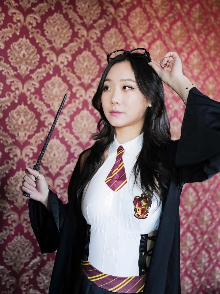 Woman wearing a Gryffindor school robe, striped tie, and wand.