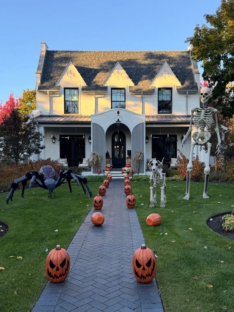 Halloween yard decorations with a giant spider, skeleton, and pumpkin-lined walkway