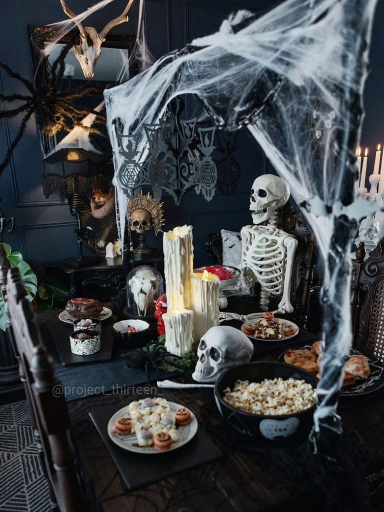 Halloween party table covered with cobwebs, snacks, and a seated skeleton