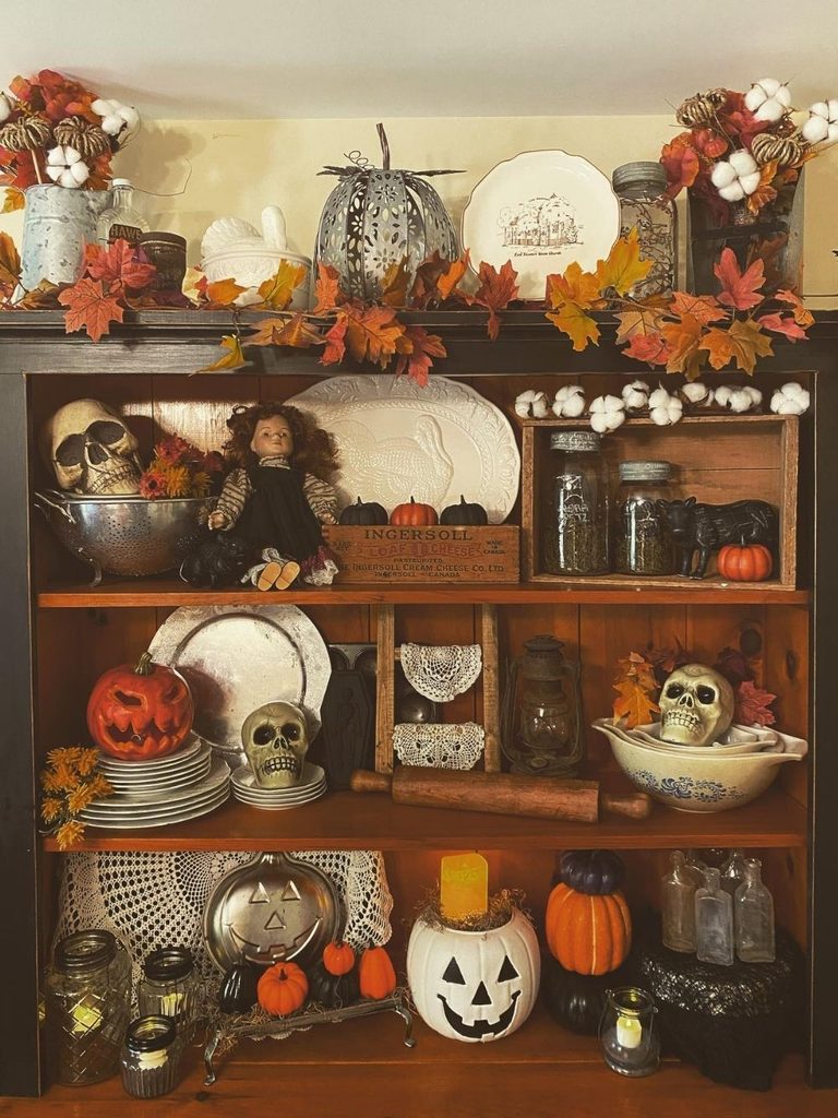 Vintage Halloween decor with skulls, pumpkins, and dried leaves on a hutch