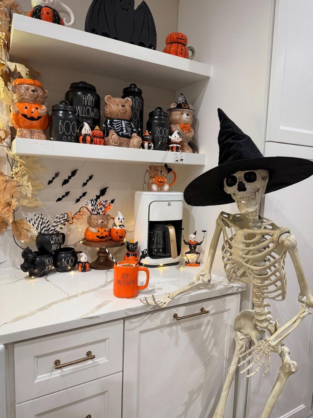 Kitchen shelf displaying Halloween mugs, figurines, and a witch-hatted skeleton