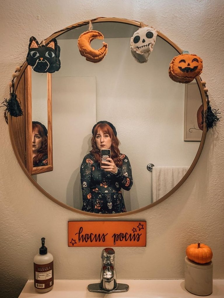 Bathroom mirror decorated with a felt garland of a cat, moon, skull, and pumpkin