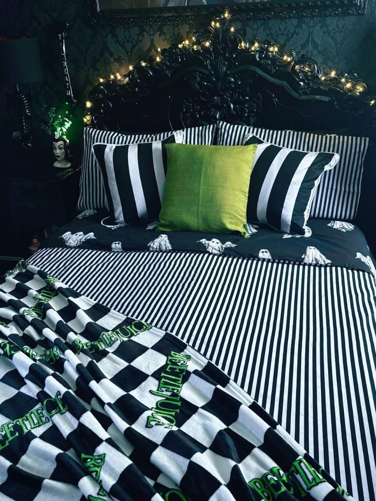 Gothic bedroom with an ornate black headboard, string lights, and a Beetlejuice-inspired throw