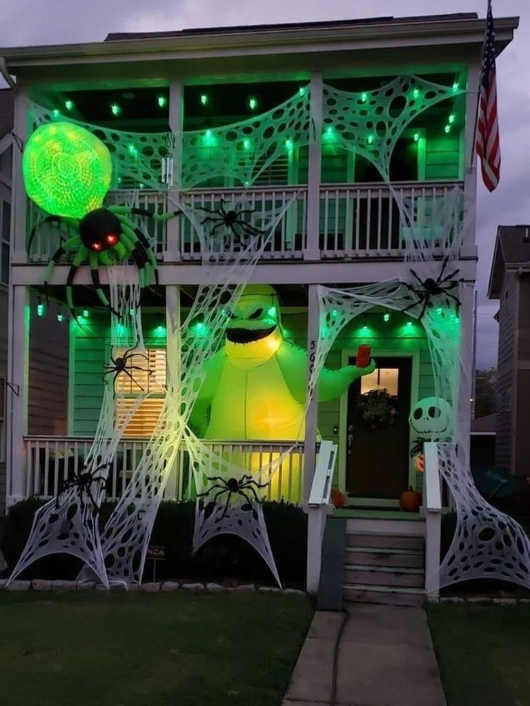 Porch with a large green inflatable character and illuminated spiderwebs