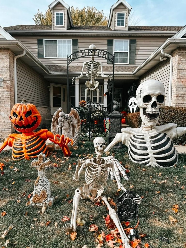 Creepy front yard decorations with a cemetery gate, skeletons, and an angel statue