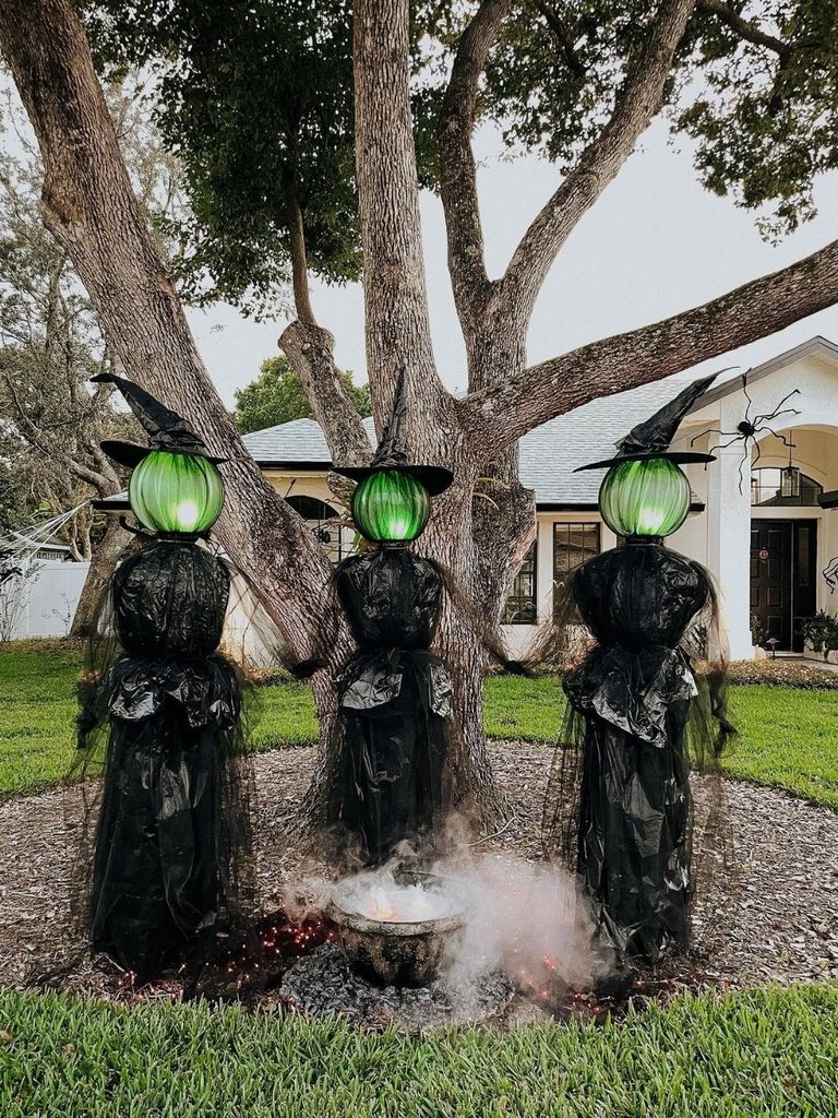 Halloween yard display with glowing witch figures gathered around a smoking cauldron