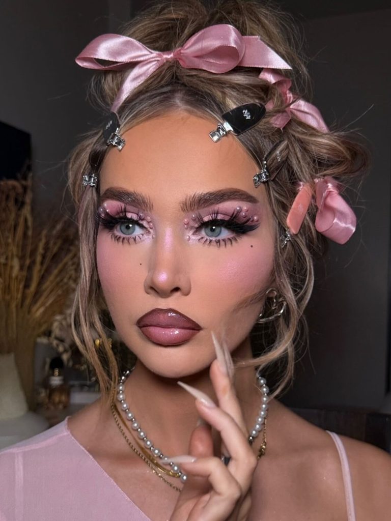 Pink pearl accents at the inner eye corners, rosy cheeks, and glossy lips create soft, pretty Halloween makeup inspired by a doll.
