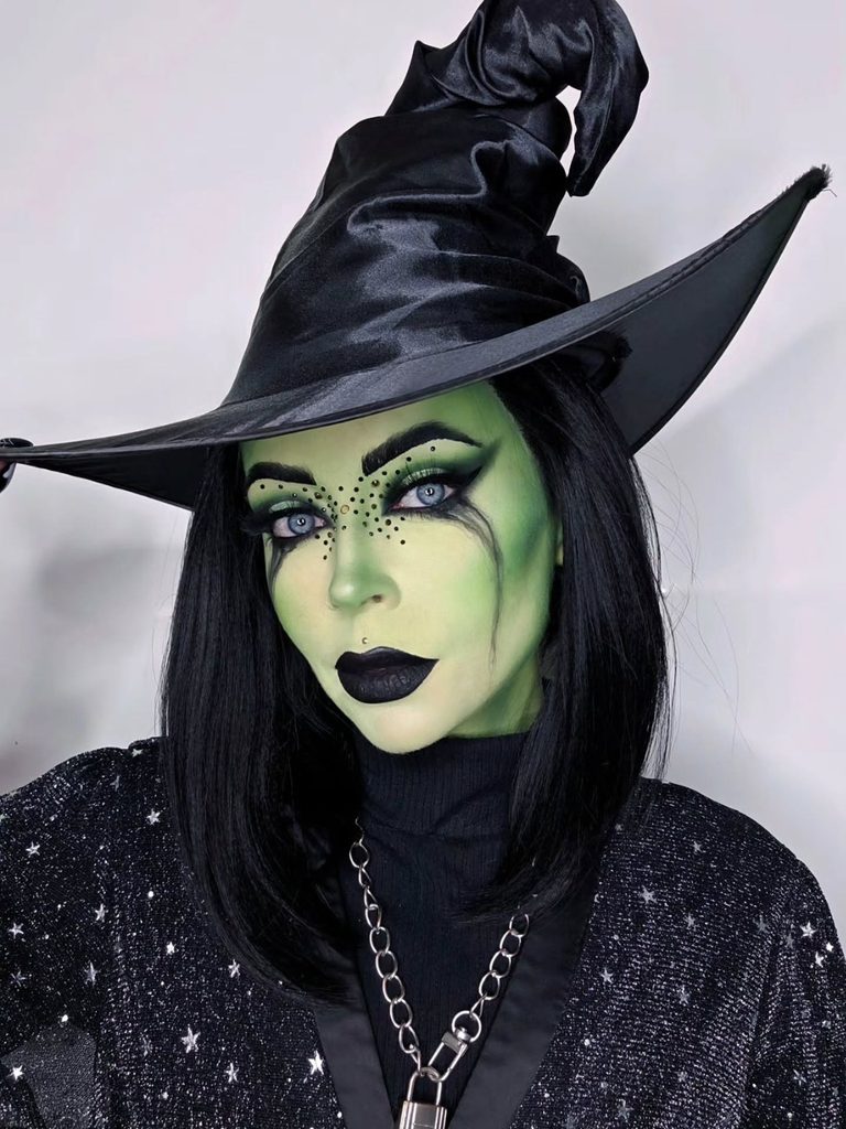 Green face paint, rhinestone freckles, and deep black lipstick make this dramatic Halloween witch makeup stand out.