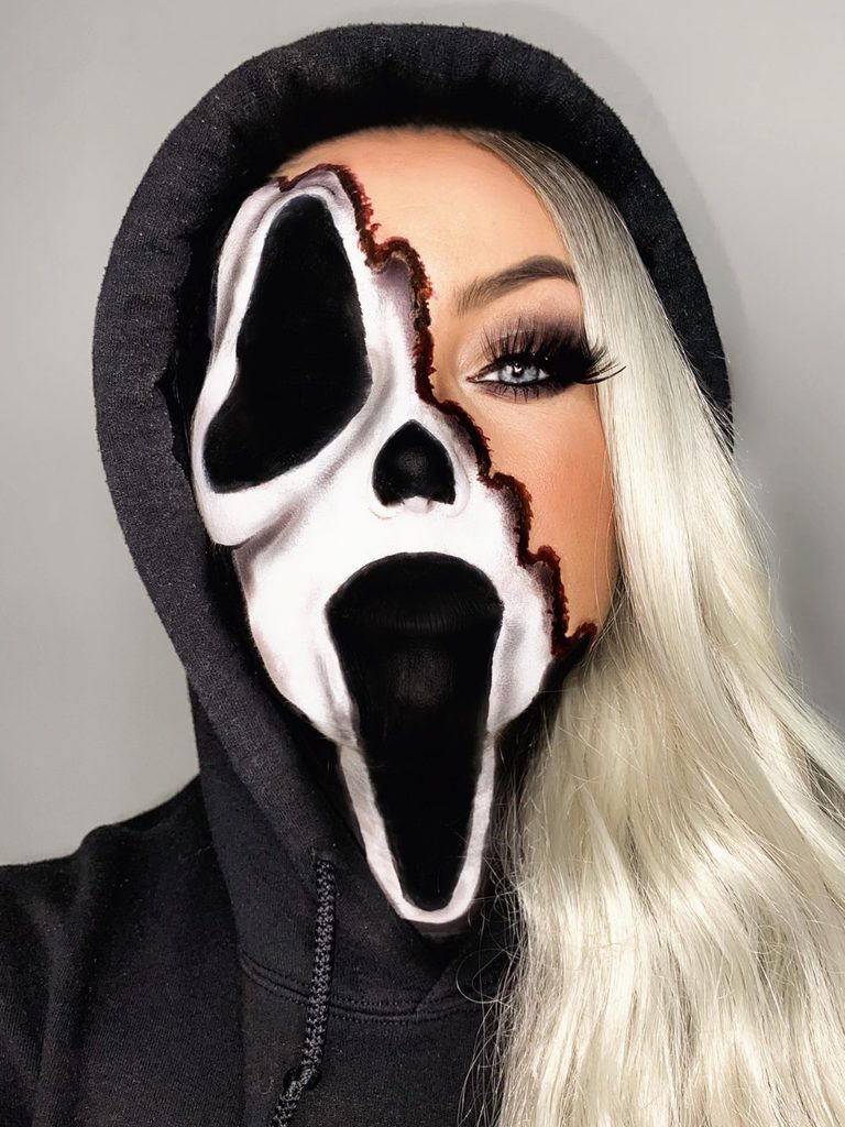 A black-and-white horror mask design on one side of the face contrasts with soft glam makeup in this half-Ghostface look.