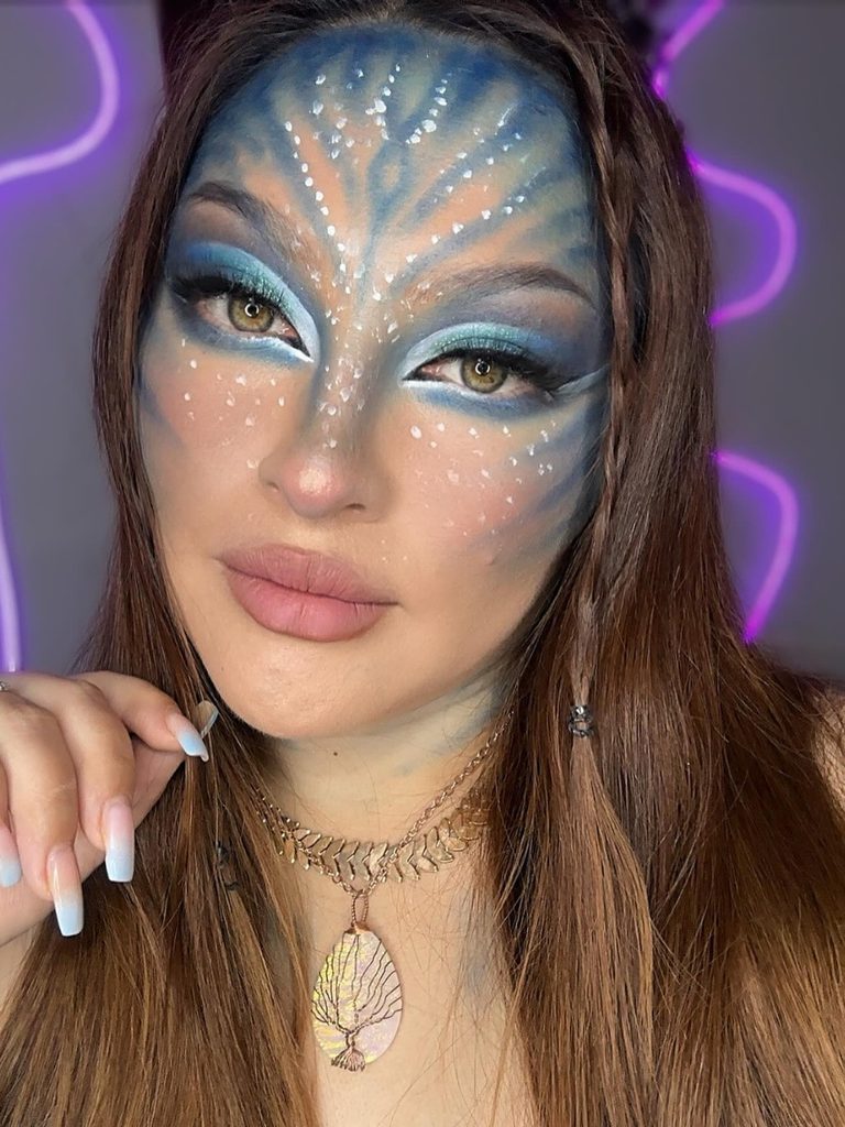Blue fern-like face markings, white freckles, and soft blue eyeshadow create this Avatar-inspired Halloween makeup look, inspired by the iconic Na’vi from the movie Avatar.