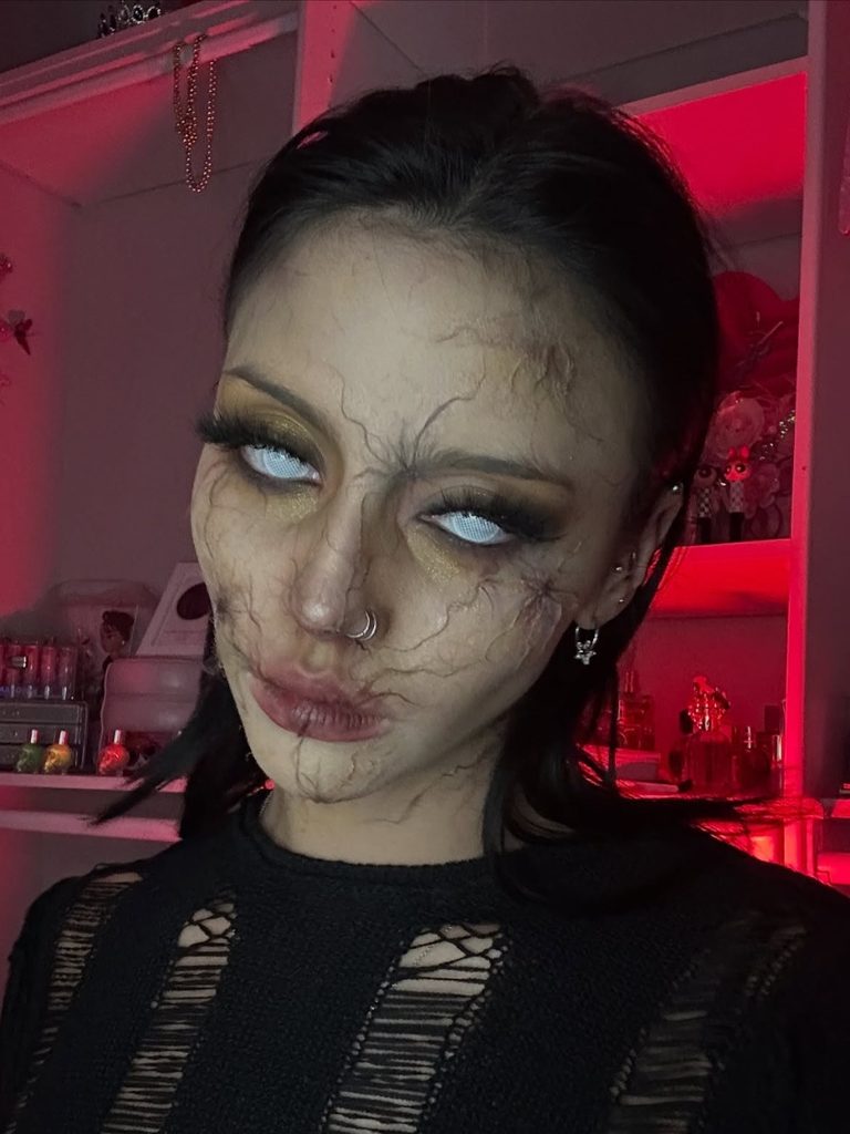 Pale, mottled skin, painted veins, and milky contact lenses create a creepy zombie Halloween makeup look.
